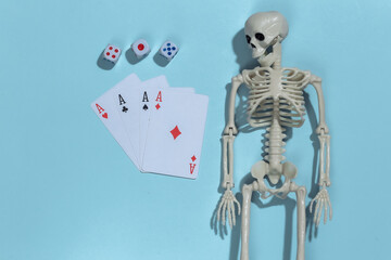 Skeleton and four aces, dice on blue background. Gambling addiction. Top view