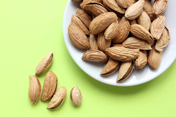 Almonds are not cleaned. Some nuts lie on a white plate on the right side, not fully visible. Five almond nuts lie separately on a yellow background. View from above. Food. Copy space