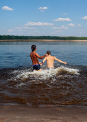 Two young men cheerfully run into the river