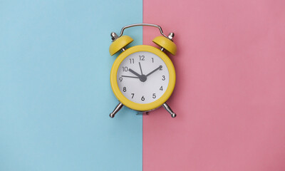 Yellow retro alarm clock on pink blue pastel background. Top view. Minimalism