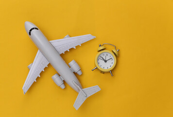 Air plane and alarm clock on yellow background. Time to travel. Top view