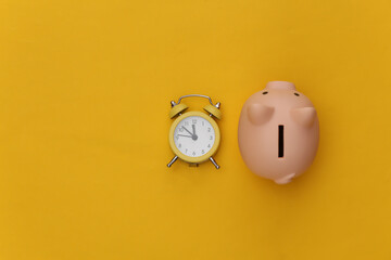 Time to invest. Piggy bank, alarm clock on yellow background. Top view. Flat lay