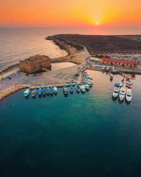 Beautiful aerial sunset shot of Paphos Castle and Paphos Harbor in Cyprus. Crystal clear water, fishing boats, luxury yachts - amazing travel destination for all year vacation. 
