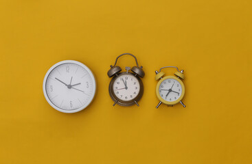 Three alarm clocks on yellow background. Top view. Flat lay