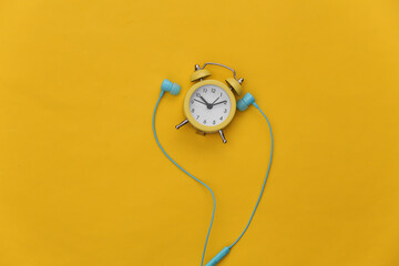 Mini alarm clock and earphones on yellow background. Top view. Flat lay