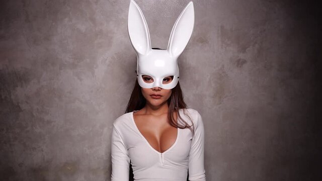 Portrait of beautiful flirting Asian woman in white dress and rabbit mask playfully posing for camera in the spotlight - video in slow motion