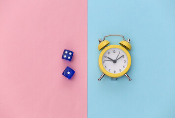 Mini alarm clock and dice on pink blue pastel background. Top view