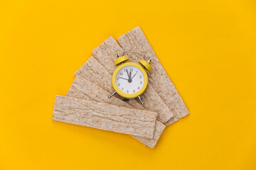 Mini Alarm clock and Diet Crispy Bread on Yellow Background. Diet Time. Top view