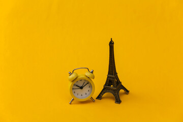 Alarm clock and eiffel tower figurine on yellow background