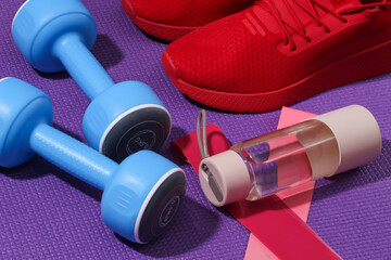 Red sports shoes, bottle water, dumbbells, fitness rubber bands on purple sports mat. Workout concept.