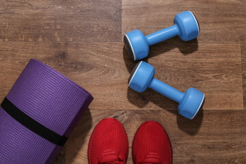 Red sports shoes, dumbbells, fitness rubber bands, mat on wooden floor. Workout concept. Top view. Flat lay