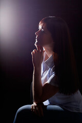 Emotional portrait of caucasian brunette girl or middle aged woman with long dark hair in blue shirt on black background and interesting light from flash in studio.