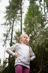 Portrain of young cute blonde girl playing and having fun on walk in forest outdoors. Happy female child posing on nature landscape with with pine trees.