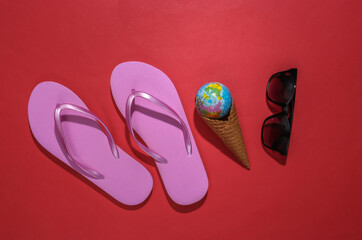 Flip flops, ice cream waffle cone with globe, sunglasses on red background. Summer flat lay. Top view