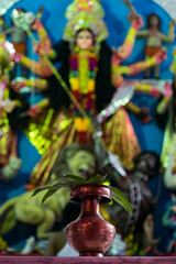 Red metallic lota with mango leaves on top in front of devi durga during durgapuja