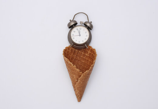 Ice cream waffle cone with alarm clock on white background. Top view