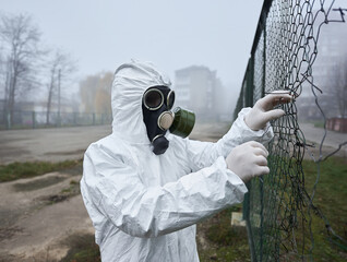 Close up of male scientist tearing torn wire fence. Man in gas mask and protective costume standing...