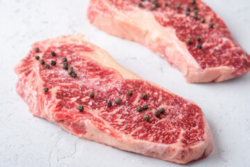 Fresh marble steaks with salt and pepper prepared for grilling on a white stone table