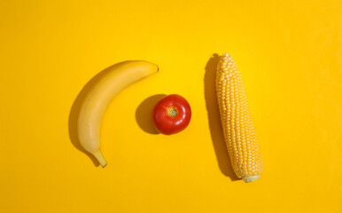Swing of corn, tomato and banana on yellow bright background. Top view