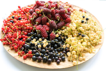 Berries of red blackberries surrounded by multi-colored currants on a wooden plate