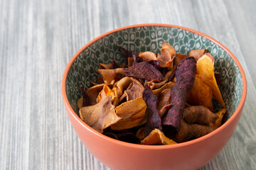 Sweet potato, beetroot and parsnip crisps chips in a patterned bowl.  Grey wood background