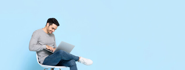 Work from home concept portrait of happy young handsome Caucasian man sitting and using laptop in isolated banner blue background with copy space