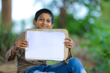 Fototapeta premium Cute little Indian/Asian boy showing writing pad pad with pen