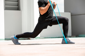 Athletic man doing lunge workout exercise with resitance band outdoors on building rooftop in the sun