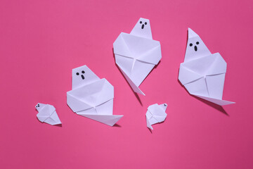 Origami ghosts on pink bright background. Handmade halloween decor. Top view