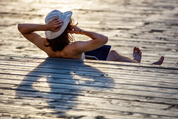 A guy in a panama hat works at a laptop while lying on a wooden podium in the park