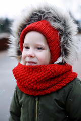 Portrait of cute sweet little girl in warm outerwear clothing outdoors in cold snowy weather
