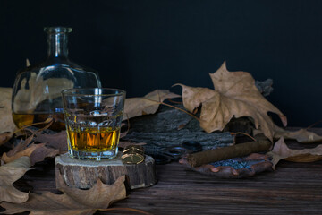 A glass of whiskey on a stand with a lighter, a cigar with an ashtray and a bottle of alcohol lie...