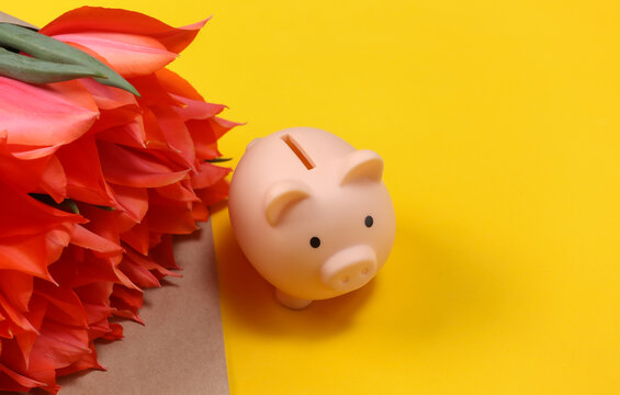 Bouquet of red tulips and piggy bank on yellow background. Holiday Mother's Day or March 8th, birthday.