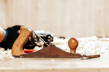 A black   jack plane is on a wooden table, next to a wooden sawdust in the workshop