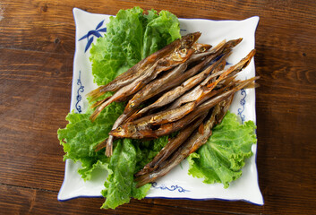 Smoked smelt and green salad leaves on a beautiful plate that stands on a wooden table. 