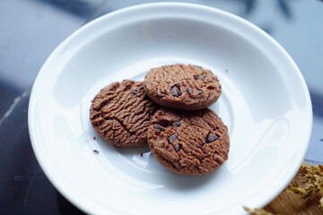 chocolate cookies and dark chocolate grain on white plate. snack theme on wooden table background