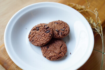 chocolate cookies and dark chocolate grain on white plate. snack theme on wooden table background