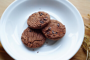 chocolate cookies and dark chocolate grain on white plate. snack theme on wooden table background