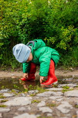 Child. A little boy in a green jacket and red boots plays in the swamp.
Carefree childhood. Happy child concept. Happy childhood.
He screams and laughs, has fun outside in the swamp.