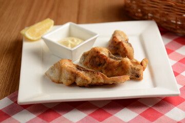 Fried fish with lemon and sauce served on white plate over wooden table with plaid tablecloth in restaurant.