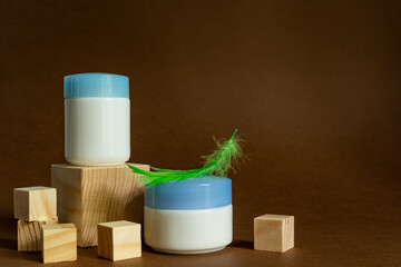 wooden podium cube display with crem jars on a brown background with green fluffy feather. Face care containers. Cosmetics mockup. Day and night products