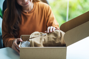 A beautiful young woman receiving and opening a postal parcel box of clothing at home for delivery and online shopping concept