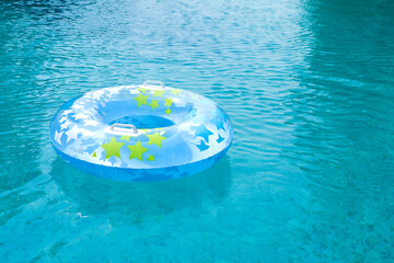 Fototapeta na wymiar Blue and yellow pool float, ring floating in a refreshing blue swimming pool. Empty swimmig pool. Copy space banner.