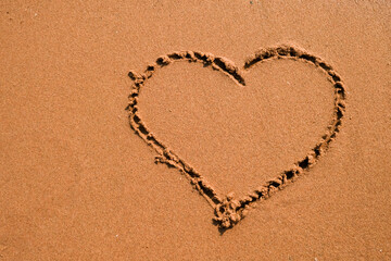 Heart drawn on sand, seacoast. Golden sand beach close up, summer holidays border frame concept.