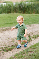 Cute little boy walking along the path on the background of reeds. Walk in park. Family life.
