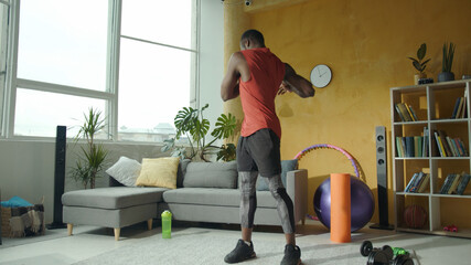 Fototapeta na wymiar Determined young african athlete working out at home, doing warming-up arm circles exercises before training. Self isolation. Bodycare, health, sports concept.