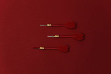 Three plastic darts with metal tip on red background. Top view. Flat lay