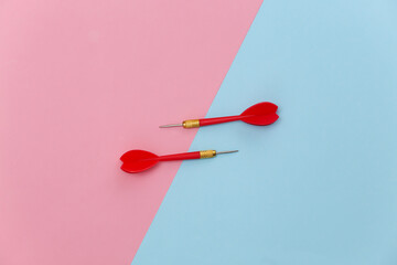 Two red plastic darts with metal tip on pink blue pastel background. Top view. Flat lay. Minimalism
