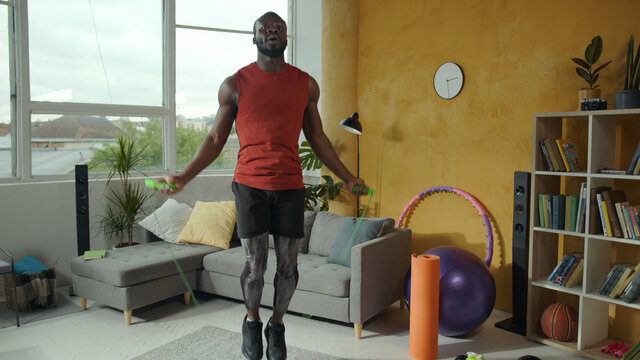 African american healthy fit athlete jumping rope in the living room. Black muscular sportsman exercising cardio workout inside apartment. Physical activity. Fitness.