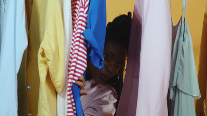 Colorful fashion clothing items hanging on store hanger. Young african attractive woman with credit hard goes through clothes selecting from rack. Vip customer.